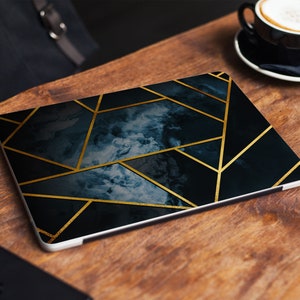 Könnte beinhalten: Ein Laptop mit einem dunkelblauen und goldenen geometrischen Design. Das Design zeigt ein marmorartiges Muster mit goldenen Linien, die ein Gitter bilden.