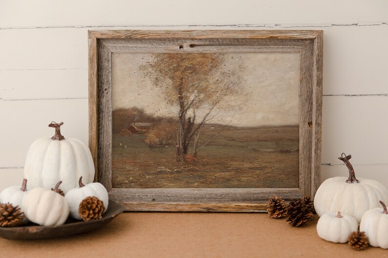 May include: A framed painting of a landscape with a tree in the foreground and a farmhouse in the distance. The painting is in a rustic wooden frame and is surrounded by white pumpkins and pine cones.