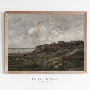 May include: A framed landscape painting depicts a coastal scene with a village atop a cliff. The artwork features a muted color palette of grays, browns, and greens, with a cloudy sky and small boats in the water. The frame is made of light-colored wood.