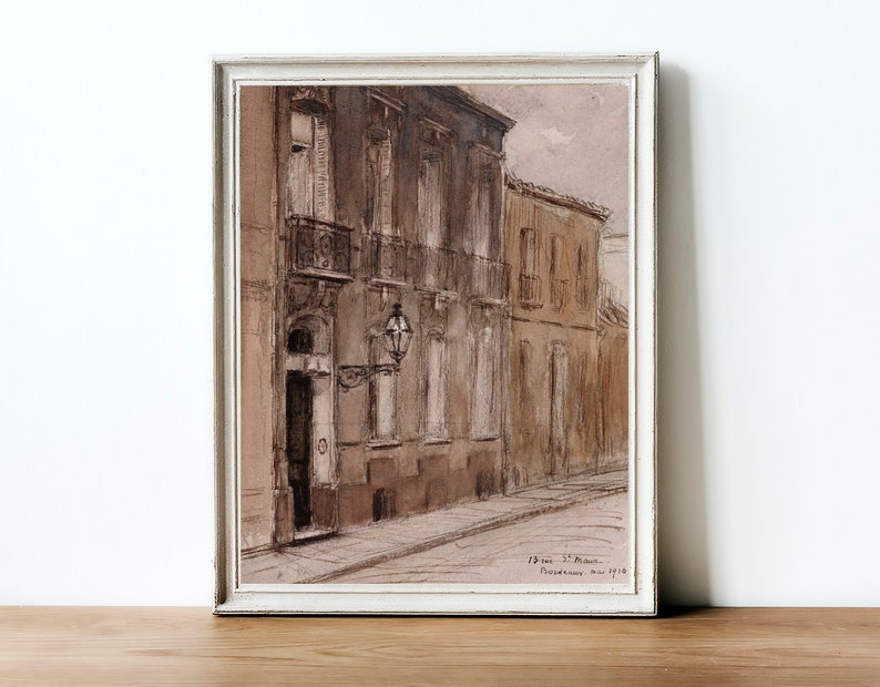 May include: A framed sepia-toned watercolor painting depicting a narrow street in a European city. The buildings are tall and have multiple windows. The street is empty and the sky is overcast.