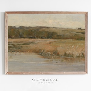 May include: A framed painting depicting a landscape scene with a body of water in the foreground, a grassy field in the middle ground, and a line of trees in the background. The sky is a light blue with some clouds.