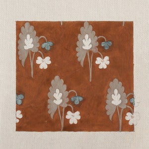 May include: A brown background with a repeating pattern of white and gray stylized flowers. The flowers have a blue center and are arranged in a symmetrical pattern.