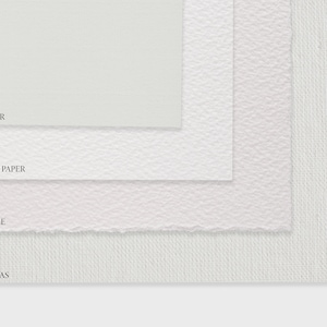 May include: Close-up of four different types of paper and canvas surfaces: fine art paper, watercolour paper, deckled edge paper, and rolled canvas. The surfaces are stacked on top of each other, with the fine art paper on top and the rolled canvas on the bottom.