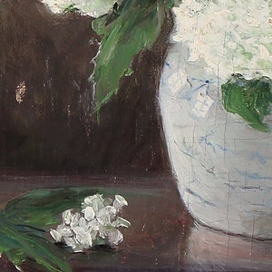 May include: A close-up of a white ceramic vase with blue and white floral designs. The vase is filled with white flowers and green leaves. A small cluster of white flowers and green leaves are on the table in front of the vase.