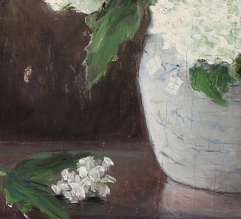 May include: A close-up of a white ceramic vase with blue and white floral designs. The vase is filled with white flowers and green leaves. A small cluster of white flowers and green leaves are on the table in front of the vase.