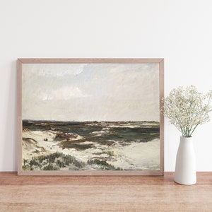 May include: A framed painting depicting a landscape scene with a cloudy sky, green grass, and white sand dunes. The painting is in a light wood frame and is hanging on a white wall.