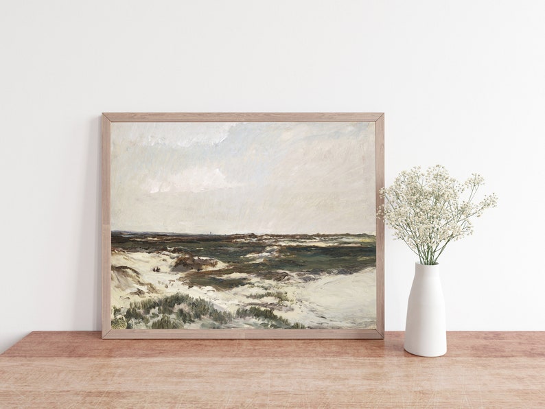 May include: A framed painting depicting a landscape scene with a cloudy sky, green grass, and white sand dunes. The painting is in a light wood frame and is hanging on a white wall.