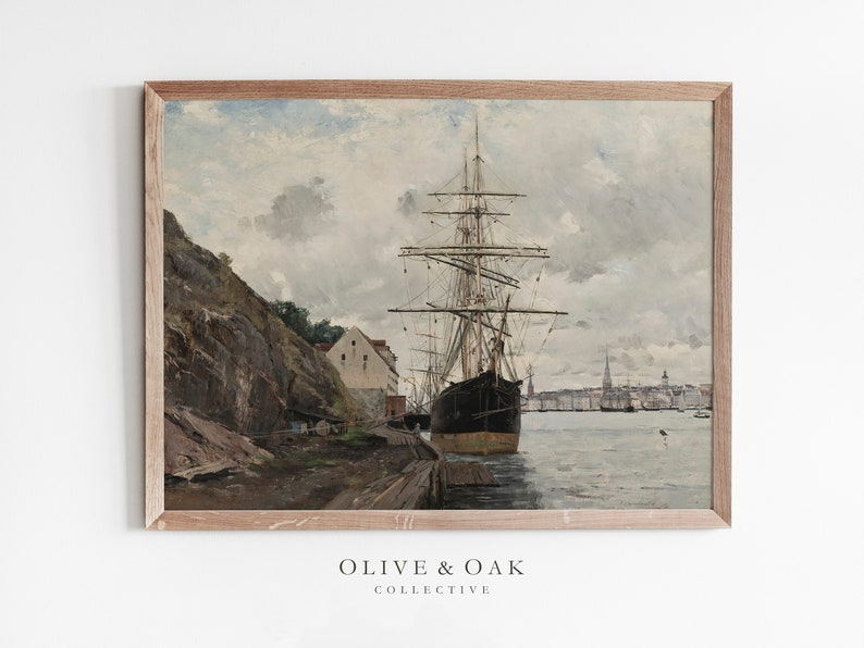 May include: A framed vintage print of a harbor scene. A large black ship is docked at a wooden pier, with a rocky cliff and buildings on the left. The sky is overcast with shades of gray and blue. The print is from the Olive & Oak Collective.
