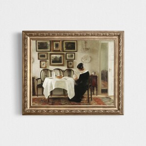 May include: A framed vintage painting shows a woman seated at a table with a white tablecloth. The room has a collection of framed pictures on the wall. The painting is in a gold-coloured ornate frame.