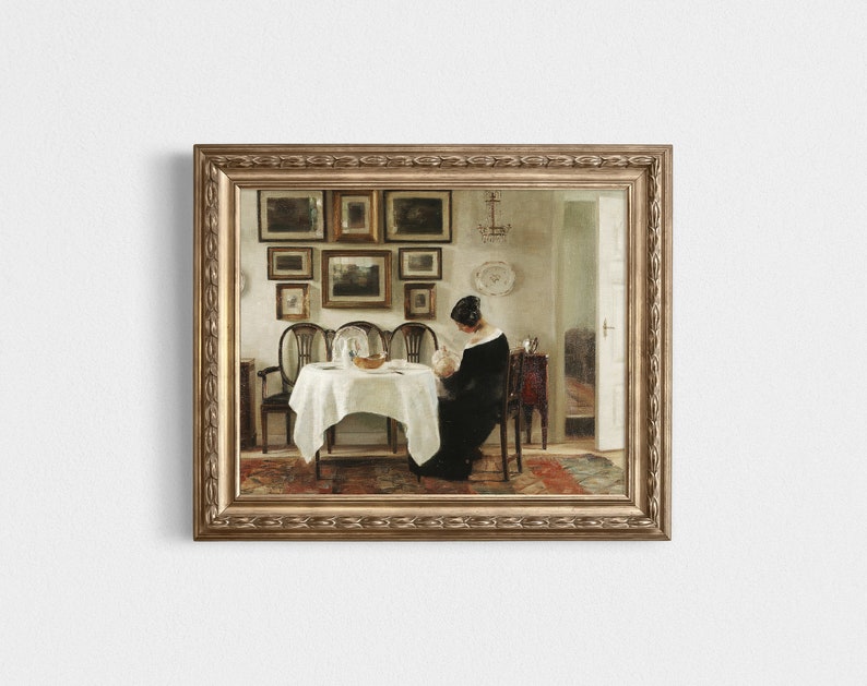 May include: A framed vintage painting shows a woman seated at a table with a white tablecloth. The room has a collection of framed pictures on the wall. The painting is in a gold-coloured ornate frame.