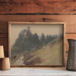 May include: A framed landscape painting depicting a misty forest scene with a winding stream in the foreground. The painting is in a rustic wooden frame and has a muted color palette of greens, browns, and grays.