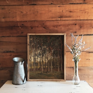 Pu&ograve; includere: Un dipinto incorniciato di una scena di bosco con alberi alti e un sottobosco verde chiaro. Il dipinto &egrave; appeso a una parete di legno con una brocca di metallo e un vaso di fiori secchi di fronte.