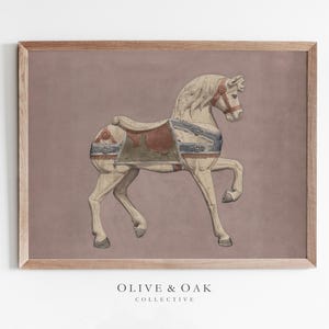 May include: A framed print featuring a vintage carousel horse illustration. The horse is cream-colored with a red and green saddle and blue accents. The background is a muted mauve, and the frame is a light brown. The text "OLIVE & OAK COLLECTIVE" is at the bottom.