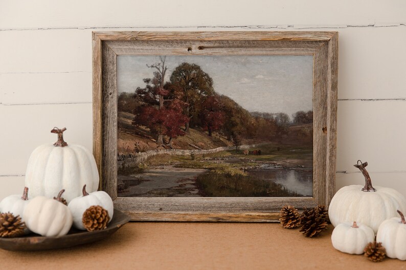 Puede incluir: Una pintura enmarcada de un paisaje rural con un r&iacute;o, &aacute;rboles y un muro de piedra. La pintura est&aacute; en un marco de madera r&uacute;stico y se exhibe en una mesa con calabazas blancas.
