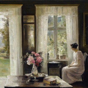 May include: A woman sits by a window in a room with white curtains. A bouquet of pink flowers in a vase sits on a wooden table with a book and a silver bowl. The window looks out onto a garden with greenery.