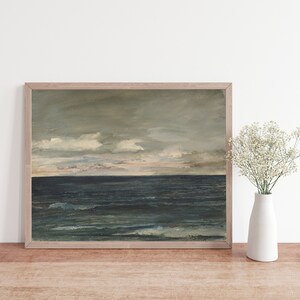 May include: A framed painting of a seascape with a dark blue ocean and a cloudy sky. The painting is in a light wood frame and is hanging on a white wall.