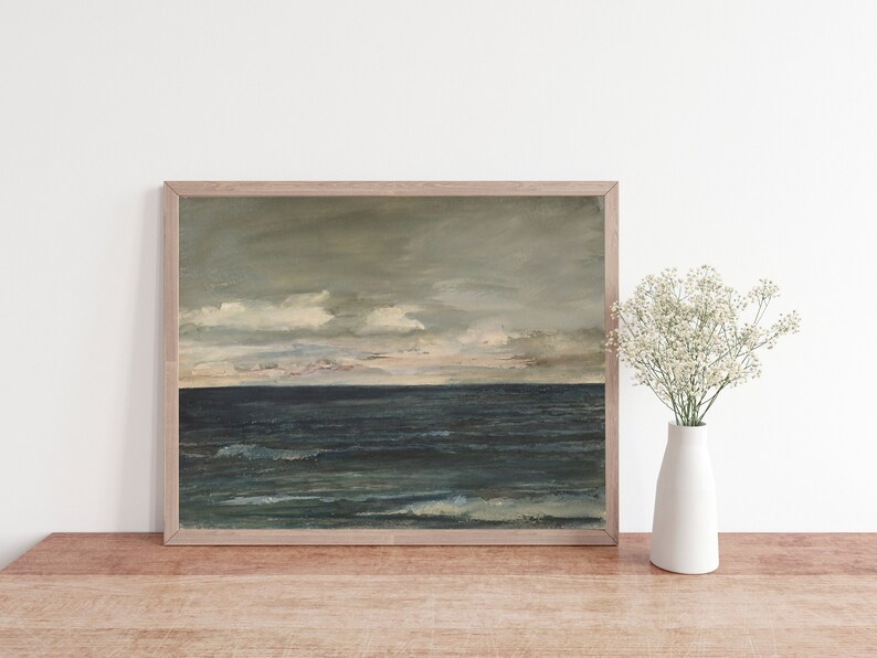 May include: A framed painting of a seascape with a dark blue ocean and a cloudy sky. The painting is in a light wood frame and is hanging on a white wall.