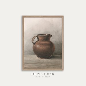 Może przedstawiać: Brązowy dzban ceramiczny z dwoma uchwytami stoi na drewnianej powierzchni na tle jasnoszarego tła. Dzban ma prosty, rustykalny design z zaokrąglonym korpusem i szerokim otworem.