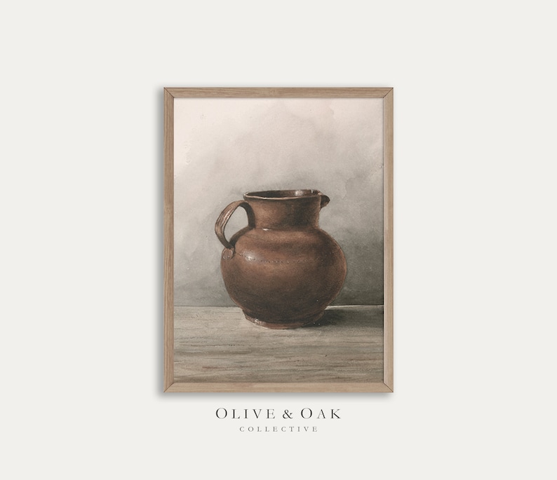 Może przedstawiać: Brązowy dzban ceramiczny z dwoma uchwytami stoi na drewnianej powierzchni na tle jasnoszarego tła. Dzban ma prosty, rustykalny design z zaokrąglonym korpusem i szerokim otworem.