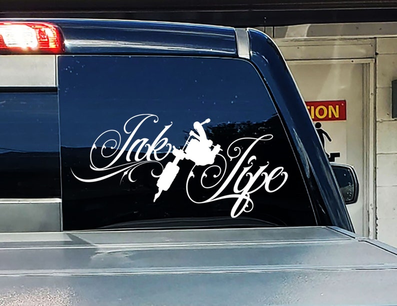 Op de afbeelding: Witte vinyl sticker met de woorden "Ink Type" in een gestileerd lettertype. In het midden van het ontwerp is een tatoeagemachine afgebeeld.