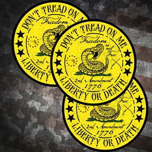 Op de afbeelding: Drie ronde gele stickers met een zwarte rand en een ratelslangontwerp. De stickers zeggen "Don't Tread On Me" en "Liberty or Death". De stickers hebben ook de tekst "2nd Amendment 1776" en "Freedom is not Free".