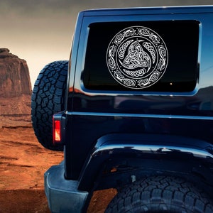 May include: A black SUV with a white Celtic knot design decal on the rear window. The decal features a circular design with a triple knot in the center.
