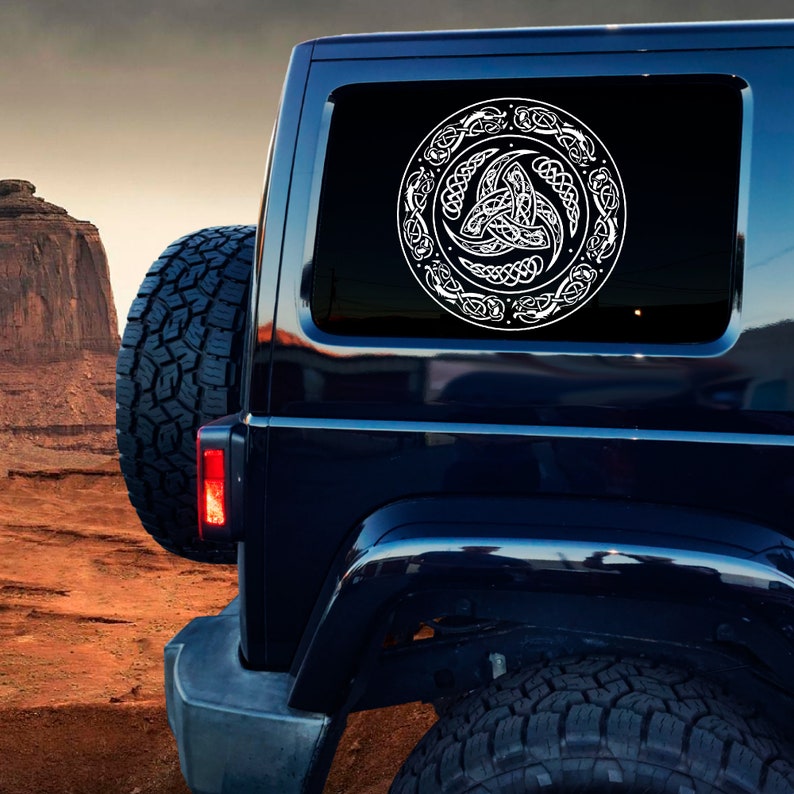 May include: A black SUV with a white Celtic knot design decal on the rear window. The decal features a circular design with a triple knot in the center.