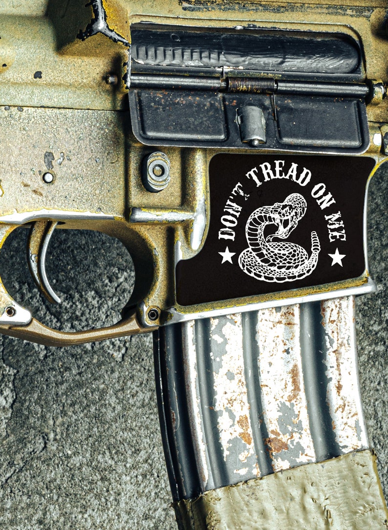 May include: A close-up of a gold-colored rifle with a black magazine and a sticker that reads "Don't Tread On Me" with a rattlesnake design.