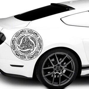 May include: A white car with a black Celtic knot design decal on the rear quarter panel. The decal is circular and features a stylized knot pattern.