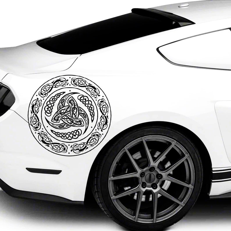 May include: A white car with a black Celtic knot design decal on the rear quarter panel. The decal is circular and features a stylized knot pattern.