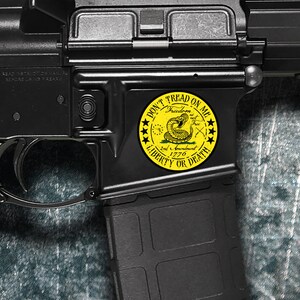 Op de afbeelding: Een zwart geweer met een gele sticker waarop "Don't Tread On Me" staat met een slang en de woorden "Freedom is not Free 2nd Amendment 1776 Liberty or Death".