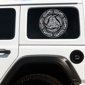 May include: White Celtic knot design car window decal on a white Jeep. The decal is a circle with a three-leaf clover knot in the center.