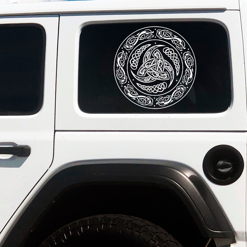 May include: White Celtic knot design car window decal on a white Jeep. The decal is a circle with a three-leaf clover knot in the center.