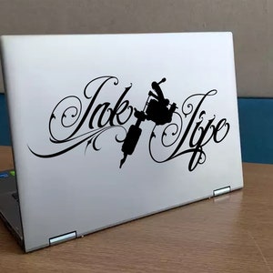 Op de afbeelding: Een witte laptop met een zwarte sticker waarop "Ink Life" staat met een gestileerd ontwerp van een tatoeagemachine.