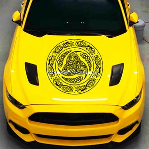 May include: A yellow car with a black and white Celtic knot design on the hood. The design is a circle with a triskelion in the center.