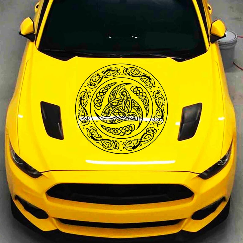 May include: A yellow car with a black and white Celtic knot design on the hood. The design is a circle with a triskelion in the center.