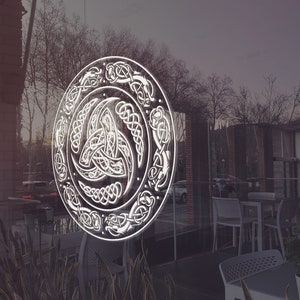 May include: A white Celtic knot design on a glass door. The design is circular and features a triskelion, a symbol of three interlocked spirals.
