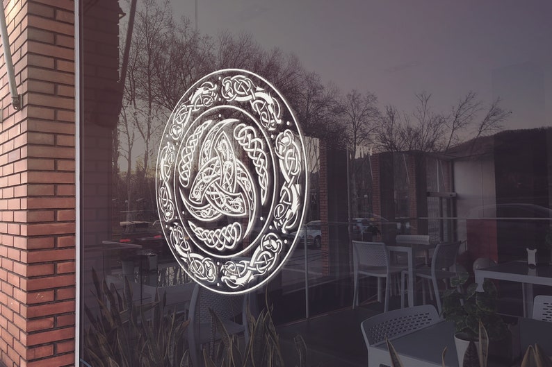 May include: A white Celtic knot design on a glass door. The design is circular and features a triskelion, a symbol of three interlocked spirals.