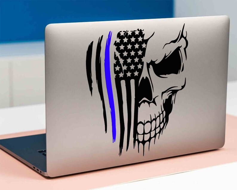 May include: A black and white skull sticker with a blue line and an American flag design. The sticker is on a silver laptop.