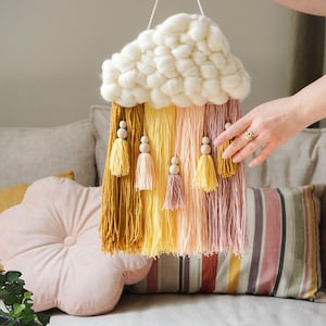 May include: A white yarn cloud wall hanging with yellow, orange, and pink yarn tassels and wooden beads.
