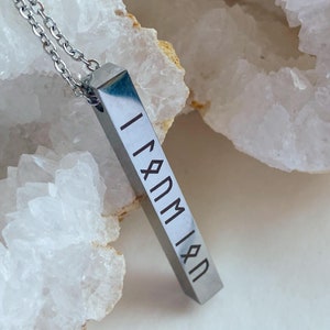 Può includere: Una collana a barra d'argento con una catena e un ciondolo inciso con rune. Il ciondolo è appeso a una roccia di cristallo bianco.