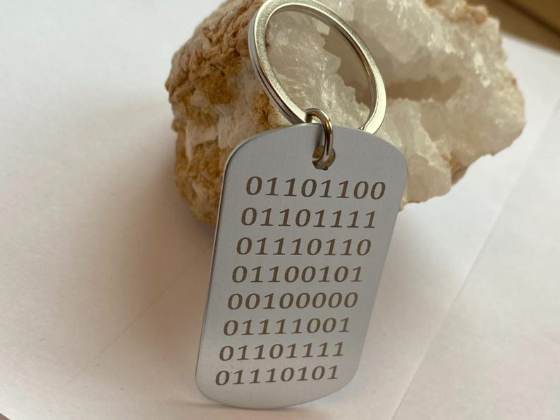 K&ouml;nnte beinhalten: Silberner Schl&uuml;sselanh&auml;nger mit einem silbernen Anh&auml;nger, der mit einer Reihe von Bin&auml;rcode-Zahlen graviert ist: 01101100, 01101111, 01110110, 01100101, 00100000, 01111001, 01101111, 01110101.