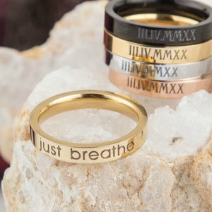 May include: A gold-colored stainless steel ring with the words "just breathe" engraved on the band.
