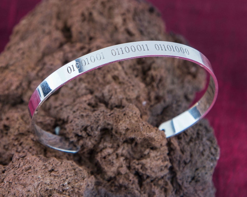 Puede incluir: Un brazalete de plata con el c&oacute;digo binario "01010001 01100011 01101000" grabado en &eacute;l.