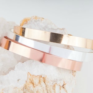 Puede incluir: Tres pulseras de metal apiladas en oro rosa, plata y oro.