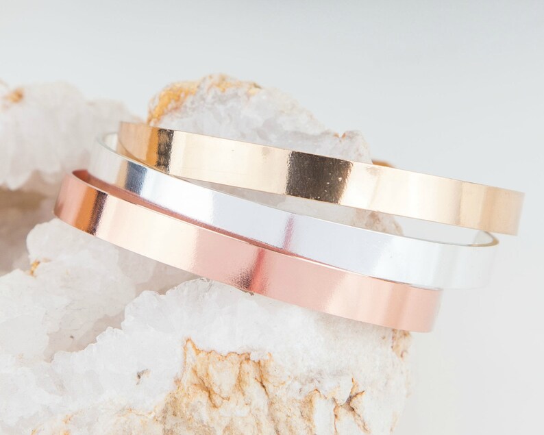 Puede incluir: Tres pulseras de metal apiladas en oro rosa, plata y oro.