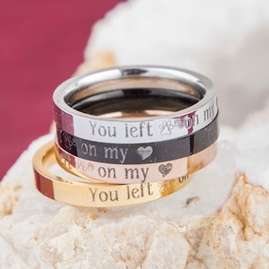 May include: Four stacked rings with a silver, black, rose gold, and gold finish. The rings are engraved with the text "You left paw prints on my heart" and a small heart symbol.