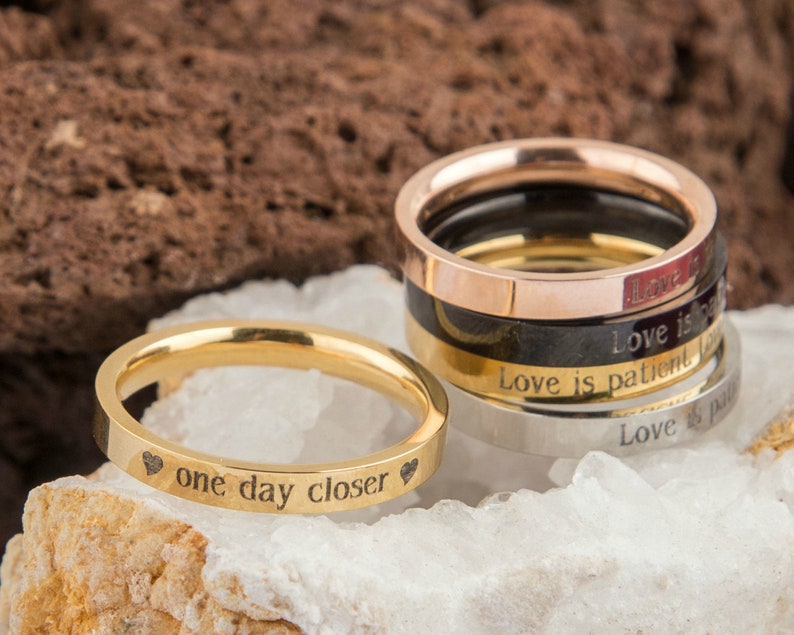 Puede incluir: Un conjunto de cuatro anillos de oro, plata, negro y oro rosa con mensajes grabados. El anillo de oro tiene la inscripci&oacute;n "one day closer" con un coraz&oacute;n a cada lado.