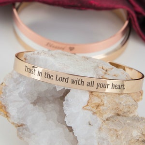 Könnte beinhalten: Goldfarbenes Armreif-Armband mit der Inschrift "Trust in the Lord with all your heart".