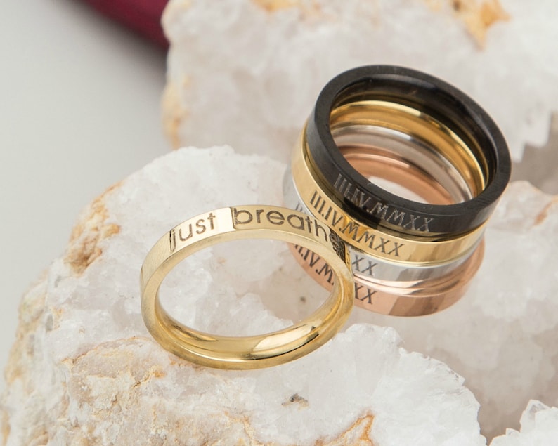 May include: A set of five gold, silver, and black rings with engraved roman numerals and the words "just breathe".